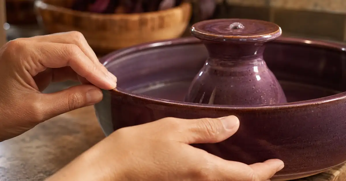 Hands inspecting the glazed surface of a ceramic pet fountain basin for chips