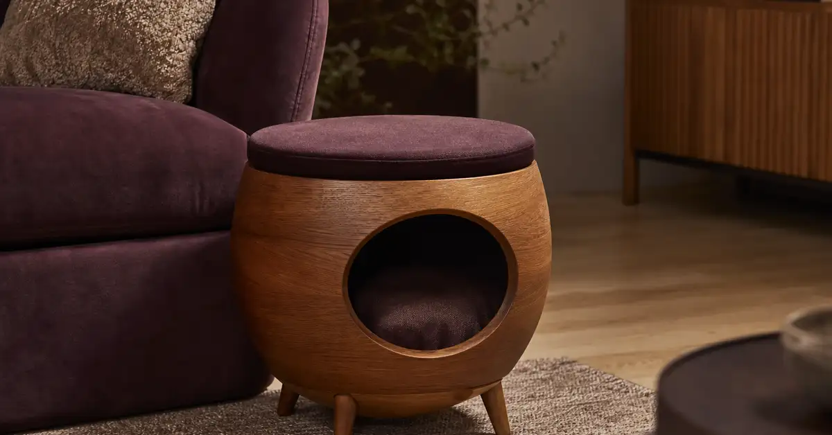 A low-profile side-table style cat furniture pod beside a sofa in a modern living room
